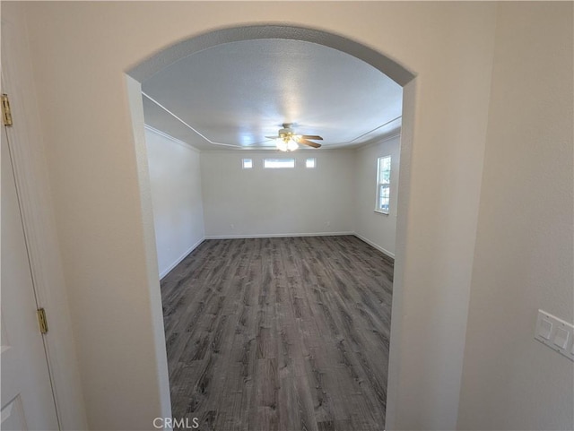 unfurnished room with arched walkways, ceiling fan, wood finished floors, and baseboards