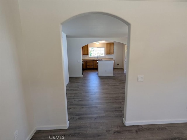 corridor with dark wood-style flooring, baseboards, and arched walkways
