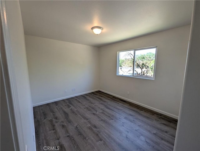 unfurnished room with dark wood-type flooring and baseboards
