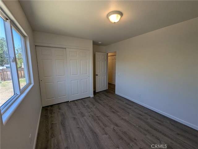 unfurnished bedroom featuring a closet, dark wood finished floors, and baseboards