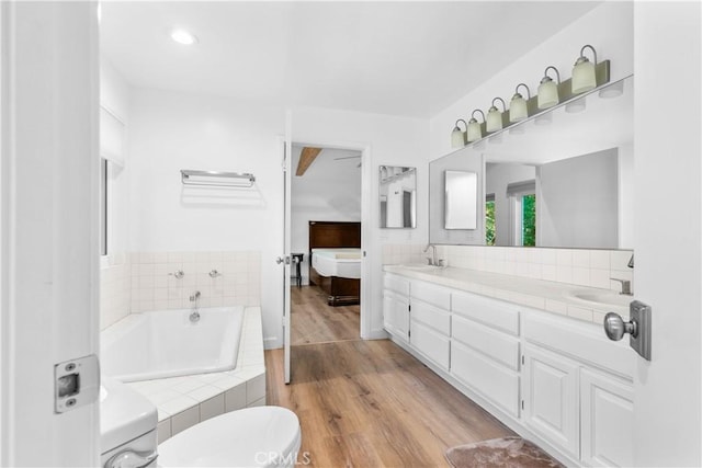full bath with a relaxing tiled tub, wood finished floors, double vanity, and a sink