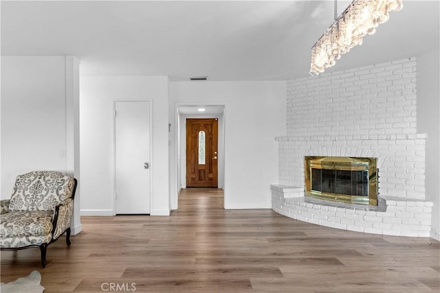 living room featuring baseboards, visible vents, wood finished floors, and a brick fireplace