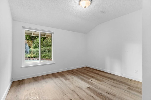 spare room with light wood-style floors, baseboards, a textured ceiling, and vaulted ceiling
