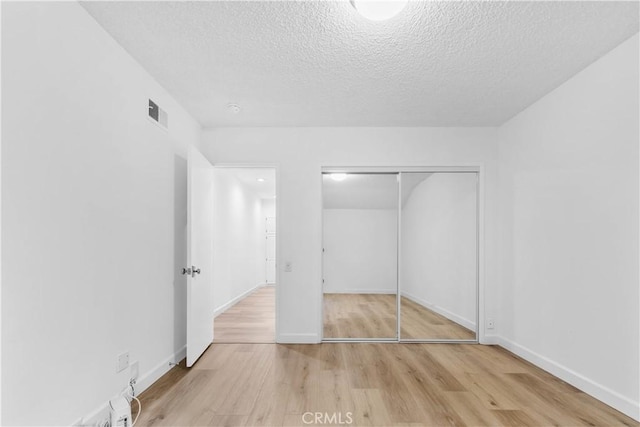 unfurnished bedroom featuring a closet, visible vents, baseboards, a textured ceiling, and wood finished floors