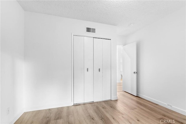 unfurnished bedroom with wood finished floors, a closet, baseboards, visible vents, and a textured ceiling
