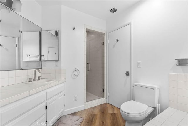 bathroom with vanity, toilet, a stall shower, visible vents, and wood finished floors