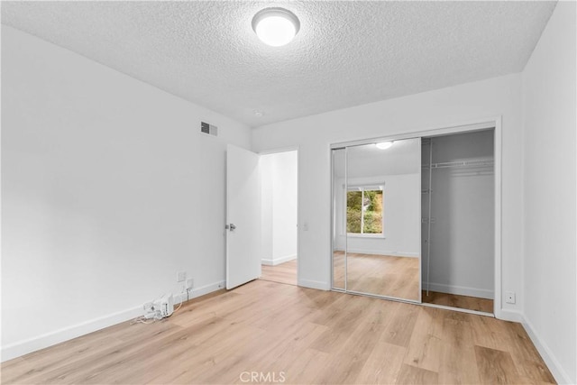 unfurnished bedroom featuring a closet, visible vents, baseboards, a textured ceiling, and wood finished floors