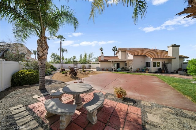 rear view of house featuring a chimney, a fenced backyard, stucco siding, and a tiled roof