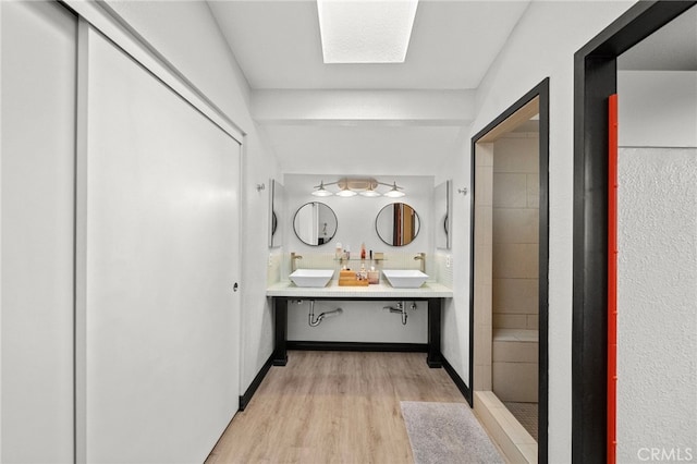 full bathroom with wood finished floors, tiled shower, double vanity, and a sink