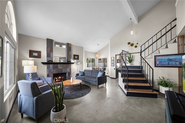 living area with a tiled fireplace, stairway, beamed ceiling, concrete floors, and high vaulted ceiling