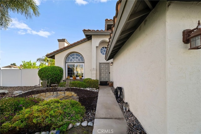 entrance to property with fence, a patio, a chimney, a tiled roof, and stucco siding