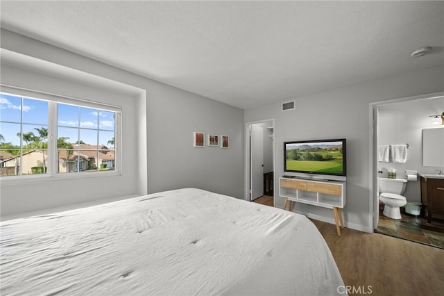 bedroom with wood finished floors, connected bathroom, baseboards, visible vents, and a textured ceiling