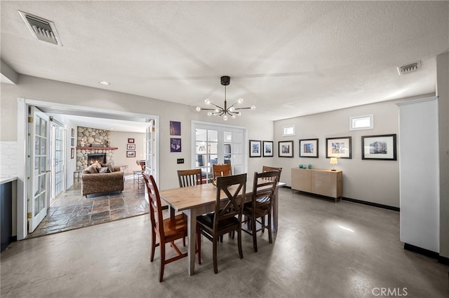 dining room featuring visible vents, a stone fireplace, a chandelier, and finished concrete floors