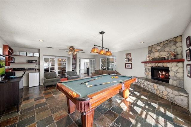 playroom with stone tile flooring, french doors, billiards, a ceiling fan, and a stone fireplace