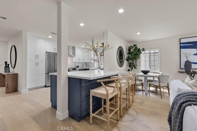kitchen featuring white cabinets, open floor plan, stainless steel fridge, recessed lighting, and wall chimney exhaust hood