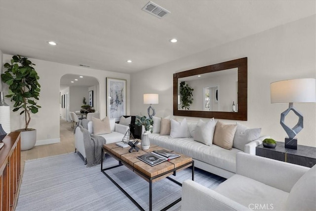 living room with arched walkways, recessed lighting, light wood finished floors, and visible vents