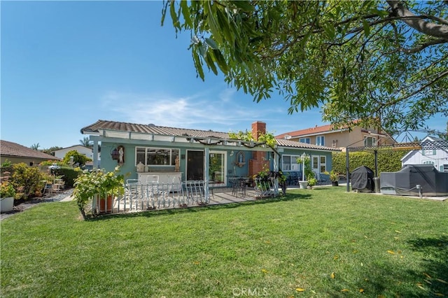 back of house featuring a lawn, a chimney, a patio area, and stucco siding