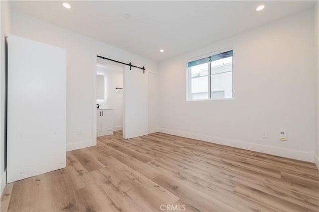 5652 La Mirada Ave, Los Angeles, CA 90038 - empty room with a barn door, light wood-style floors, recessed lighting, and baseboards
