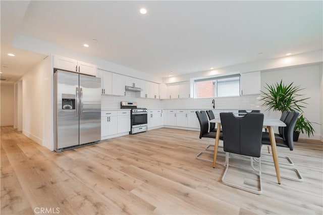 5652 La Mirada Ave, Los Angeles, CA 90038 - kitchen with appliances with stainless steel finishes, backsplash, white cabinetry, light wood-type flooring, and under cabinet range hood