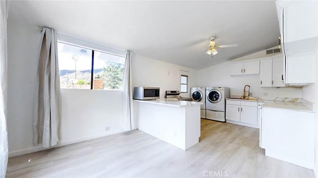 kitchen featuring a sink, appliances with stainless steel finishes, light wood-type flooring, washer and clothes dryer, and a peninsula