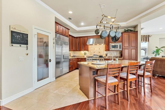 kitchen featuring built in appliances, crown molding, visible vents, and a raised ceiling