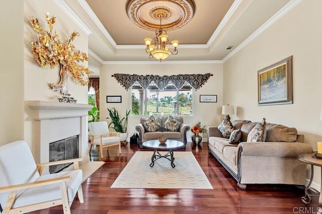 living room with crown molding, a glass covered fireplace, a tray ceiling, and dark wood-style floors
