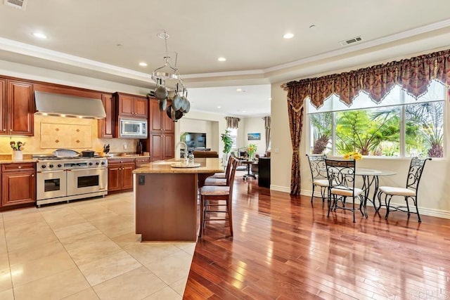 kitchen with visible vents, crown molding, a breakfast bar area, wall chimney exhaust hood, and appliances with stainless steel finishes