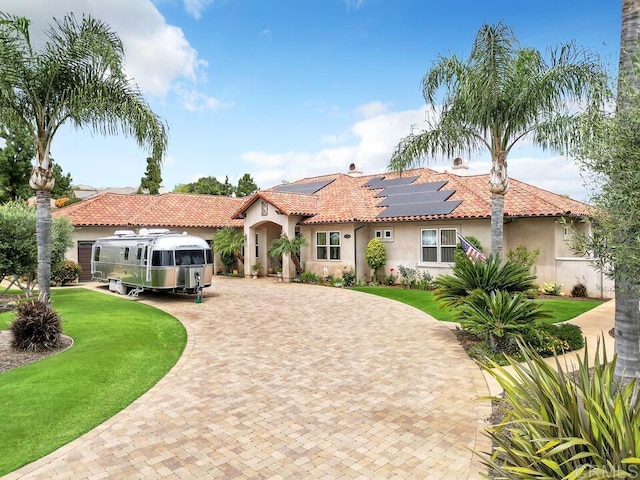 mediterranean / spanish house featuring curved driveway, stucco siding, a front yard, and solar panels