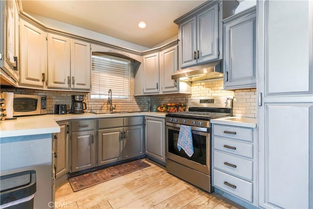 kitchen featuring stainless steel appliances, under cabinet range hood, light countertops, a sink, and gray cabinetry