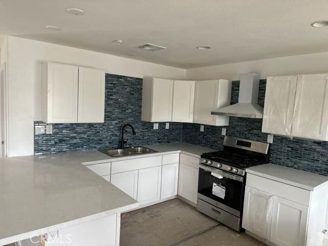 kitchen featuring wall chimney range hood, a sink, visible vents, gas stove, and a peninsula