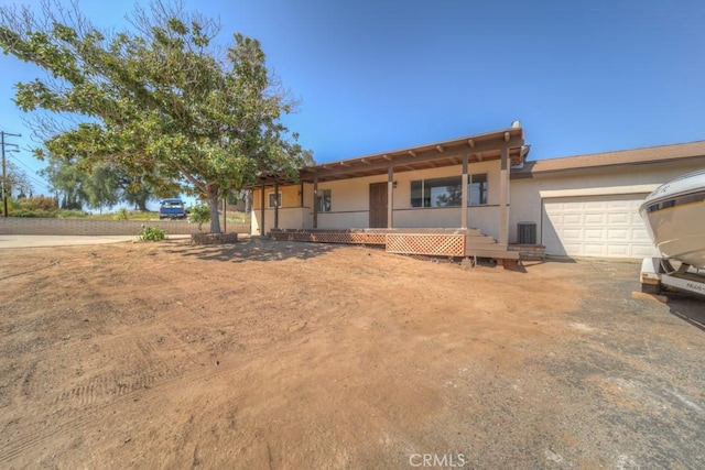 ranch-style house with covered porch, stucco siding, central AC unit, and an attached garage
