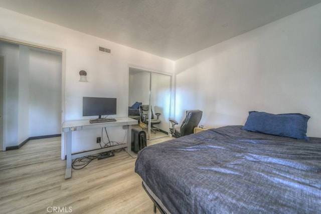 bedroom with baseboards, visible vents, wood finished floors, and a closet