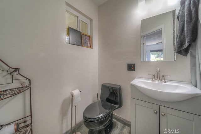 half bath featuring baseboards, wood finished floors, toilet, and vanity