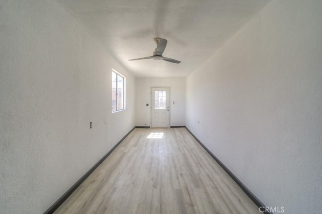 doorway featuring baseboards, a ceiling fan, and light wood-style flooring