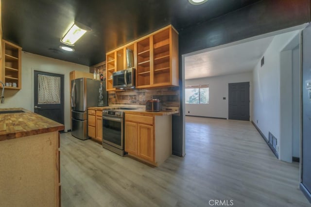 kitchen featuring butcher block countertops, decorative backsplash, stainless steel appliances, open shelves, and light wood finished floors