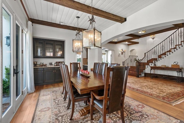dining room featuring a notable chandelier, beam ceiling, arched walkways, light wood-type flooring, and stairway