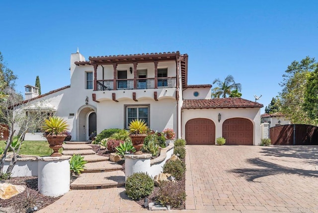 mediterranean / spanish-style home with fence, a garage, stucco siding, decorative driveway, and a balcony