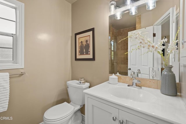 bathroom featuring toilet, tiled shower, vanity, and baseboards