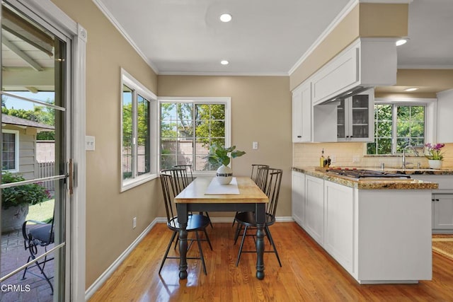 dining room with a healthy amount of sunlight, light wood-type flooring, crown molding, and baseboards