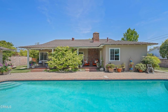 back of house featuring stucco siding, an outdoor pool, a chimney, and fence