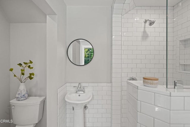 full bathroom featuring toilet, a tile shower, and tile walls
