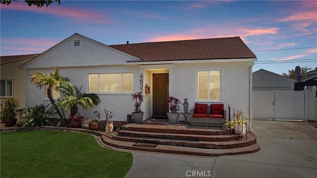 bungalow-style home with a gate, a lawn, roof with shingles, stucco siding, and fence