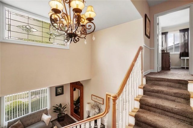 staircase featuring baseboards, an inviting chandelier, and a towering ceiling
