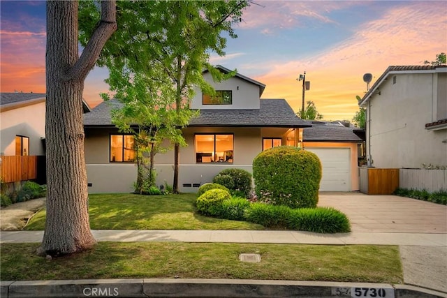 view of front of house with driveway, fence, a shingled roof, a lawn, and stucco siding