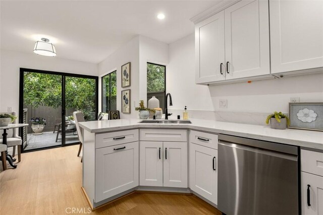 kitchen featuring dishwasher, a sink, white cabinets, a peninsula, and light wood-style flooring