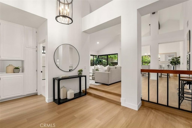 hallway with light wood-style floors, a chandelier, and high vaulted ceiling
