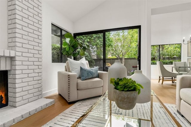living area with plenty of natural light, a brick fireplace, lofted ceiling, and wood finished floors