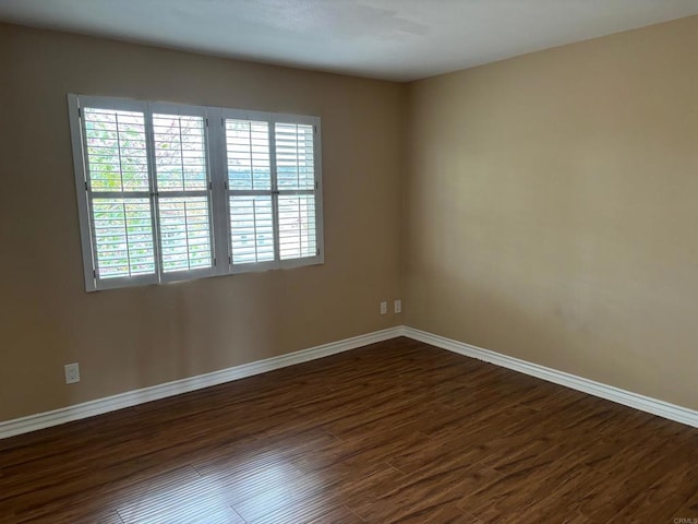 spare room featuring dark wood-style flooring and baseboards
