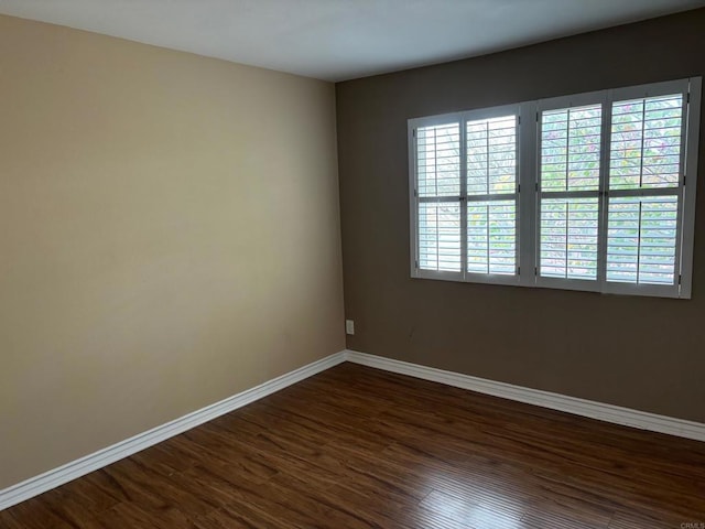spare room featuring baseboards and dark wood-style flooring