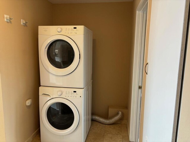 laundry room featuring baseboards, light tile patterned flooring, stacked washer / drying machine, and laundry area